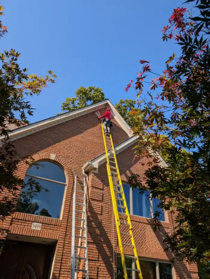 Professional installer on ladder mounting permanent lights on brick home